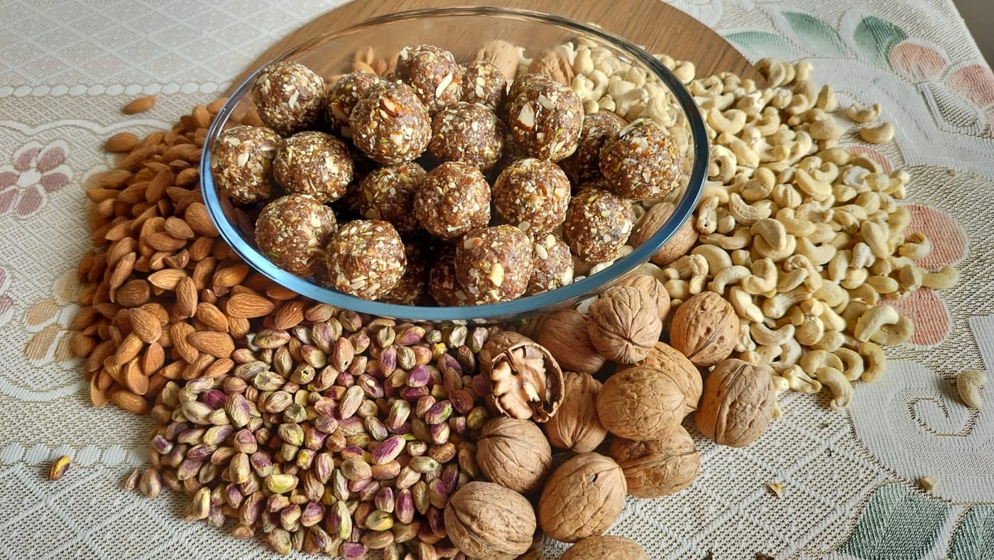 Dry-fruit laddoos in a glass bowl surrounded by almonds, cashews, pistachios and walnuts
