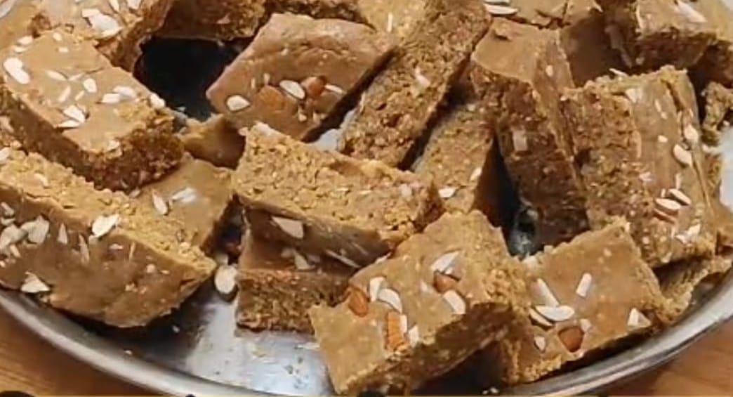 Pieces of til-mungfali kalakand topped with slivered almonds on a steel plate