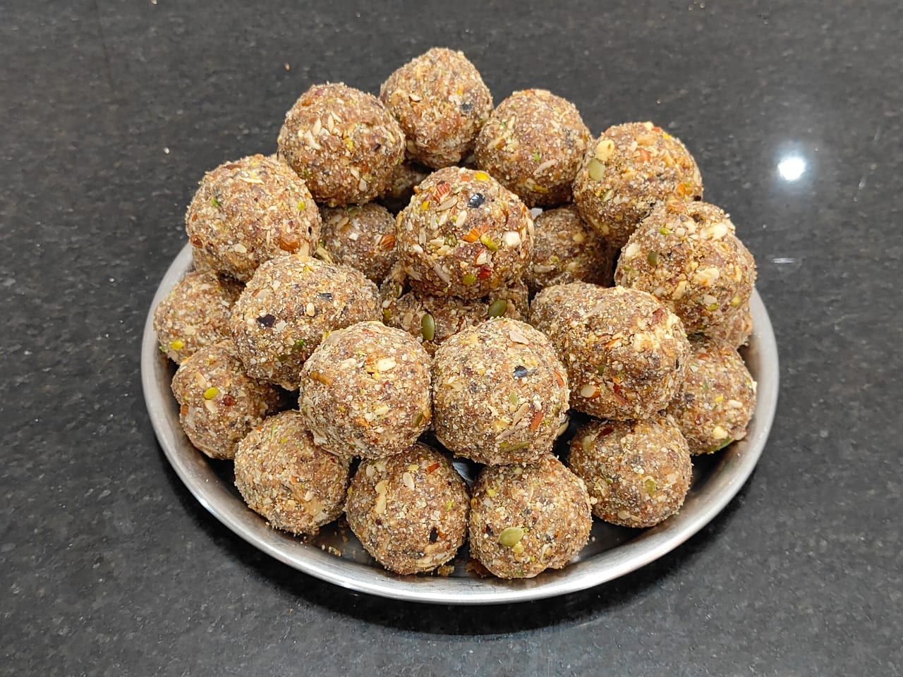 Multigrain millet laddoos studded with seeds and nuts, stacked on a steel plate
